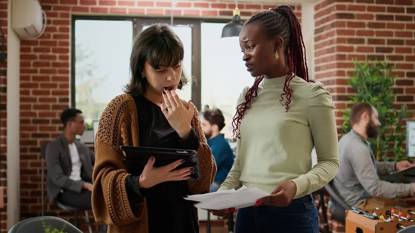 Деловые женщины анализируют информацию на бумагах и цифровом планшете, работая командой над созданием презентации стартапа. Они используют диаграммы данных для планирования партнёрского проекта и исследовательского отчёта.