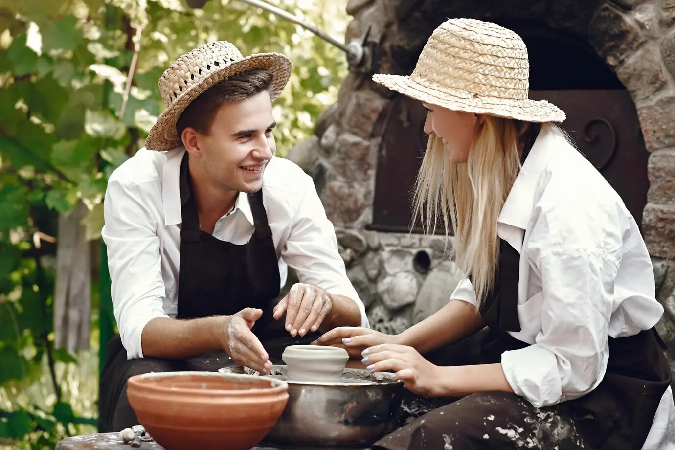 Пара в коричневых фартуках изготавливает вазу.